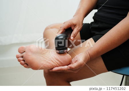 Asian woman use electric foot scrubber for treat and repair dry heel skin. 117451202