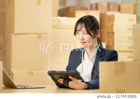 倉庫にてタブレットを使って仕事をする若い女性 物流事務 イメージ 倉庫にてタブレットを使って仕事をする若い女性 物流事務 イメージ 117451900