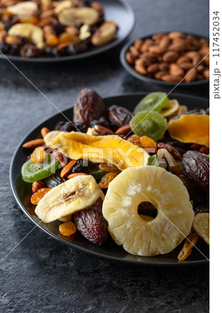 Dried tropical fruits, nuts, and raisins in black plate. 117452034