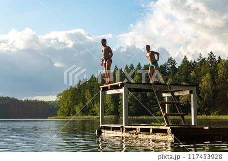 Teenage boys jumping in lake water at summer holiday. Teenage boys jumping in lake water at summer holiday. 117453928