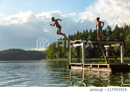Teenage boys jumping in lake water at summer holiday. Teenage boys jumping in lake water at summer holiday. 117453929