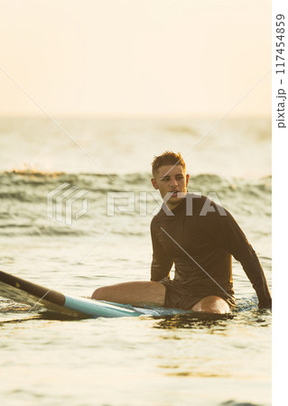 Surfer sitting on his surfboard during sunrise 117454859