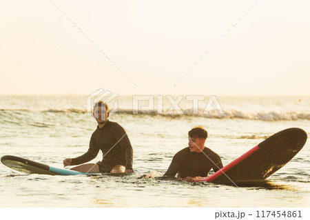 Two friends having a good time at a surf camp during their vacations 117454861