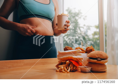 To eat or not. Cheerless plump woman looking at the burger while thinking to eat it or not To eat or not. Cheerless plump woman looking at the burger while thinking to eat it or not 117456160