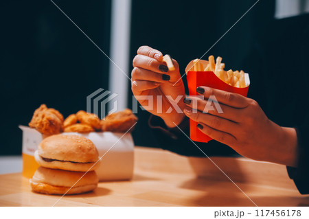 Asian woman holding french fries and eating happily in restaurant Asian woman holding french fries and eating happily in restaurant 117456178