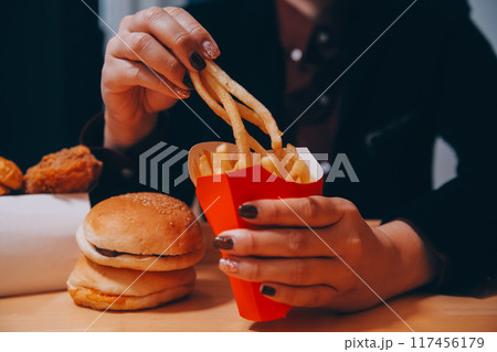 Asian woman holding french fries and eating happily in restaurant Asian woman holding french fries and eating happily in restaurant 117456179