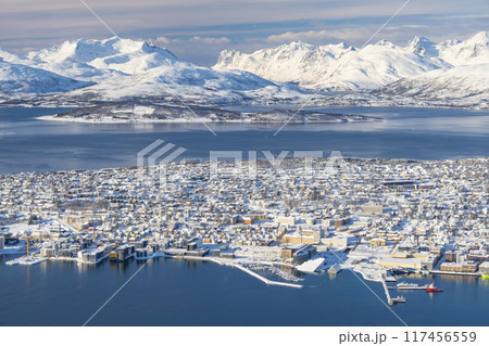 Aerial Panorama of norwegian city of Tromso in the winter. Snowy roofs, embankment near the port and fishing ships, Sunny winter day. 117456559