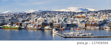 Panorama of norwegian city of Tromso in the winter. Snowy roofs, embankment near the port and fishing ships, Sunny winter day. 117456564