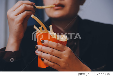 Asian woman holding french fries and eating happily in restaurant 117456750