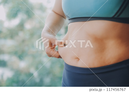 fat woman, fat belly, chubby, obese woman hand holding excessive belly fat with measure tape, woman diet lifestyle concept 117456767