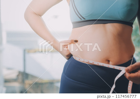 fat woman, fat belly, chubby, obese woman hand holding excessive belly fat with measure tape, woman diet lifestyle concept 117456777