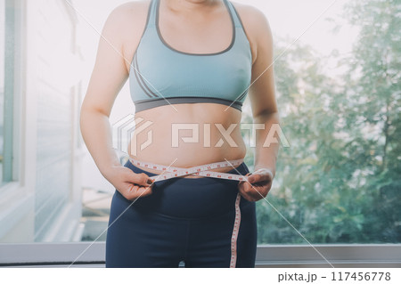 fat woman, fat belly, chubby, obese woman hand holding excessive belly fat with measure tape, woman diet lifestyle concept 117456778