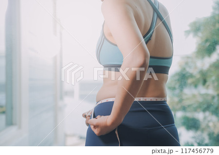 fat woman, fat belly, chubby, obese woman hand holding excessive belly fat with measure tape, woman diet lifestyle concept 117456779