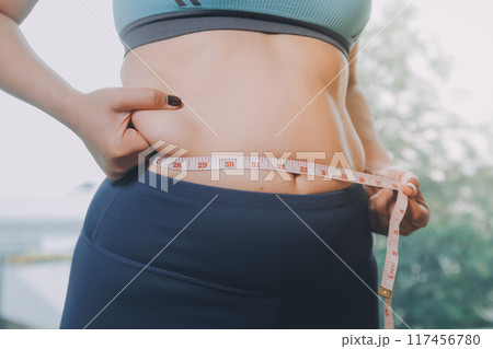fat woman, fat belly, chubby, obese woman hand holding excessive belly fat with measure tape, woman diet lifestyle concept 117456780