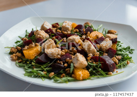 Vegetable salad with arugula, cheese, orange and beets on a white plate 117457437