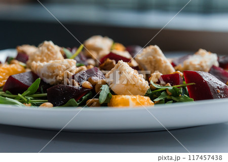 Vegetable salad with arugula, cheese, orange and beets on a white plate Vegetable salad with arugula, cheese, orange and beets on a white plate 117457438
