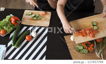 Mother and daughter preparing healthy salad in the kitchen, adding fresh ingredients into a glass bowl Mother and daughter preparing healthy salad in the kitchen, adding fresh ingredients into a glass bowl 117457794