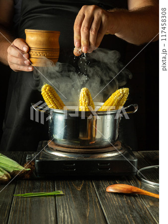 Chef salting hot corn cobs in a saucepan in the kitchen. Restaurant or hotel service concept. Maize diet menu 117458308