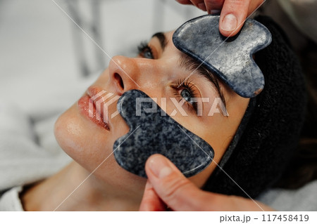 Relaxing facial treatment with gua sha stones at a spa during the day in a calm setting Relaxing facial treatment with gua sha stones at a spa during the day in a calm setting 117458419