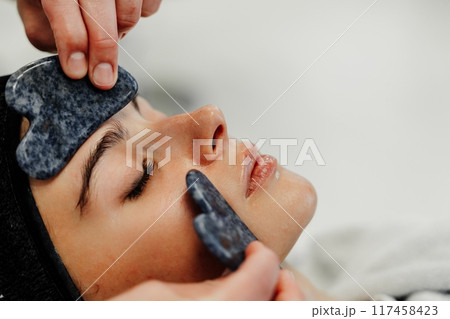 Relaxing facial treatment using gua sha tools at spa during afternoon Relaxing facial treatment using gua sha tools at spa during afternoon 117458423