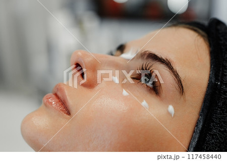 Woman receiving facial treatment with cream applied at spa during relaxing afternoon session 117458440