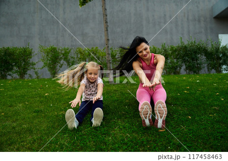 Mother and daughter exercising on the grass in a park in the afternoon sun 117458463