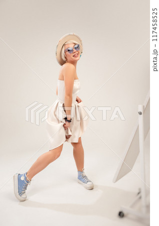 A naughty fashionable girl in a dress is fooling around and dancing in front of a mirror in a studio with a white background copy paste A naughty fashionable girl in a dress is fooling around and dancing in front of a mirror in a studio with a white background copy paste 117458525
