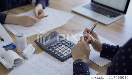 Accountants or auditors reviewing financial documents while using laptop, calculator and sitting opposite one another at the wooden desk in office. Audit and taxes 117460013