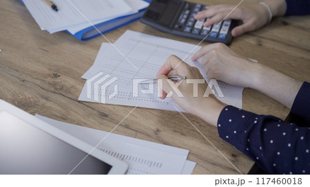 Accountants or auditors reviewing financial documents while sitting at the wooden desk in office. Professionals analyzing paper reports and using calculators, close up. Audit and taxes concept 117460018