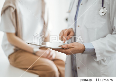 Doctor and patient in clinic. Friendly physician using tablet computer near a young woman. Medicine concept Doctor and patient in clinic. Friendly physician using tablet computer near a young woman. Medicine concept 117460070