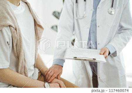 Doctor and patient in clinic. Friendly physician examining a young woman with a one hand while keeping a clipboard with medical records in another. Medicine concept Doctor and patient in clinic. Friendly physician examining a young woman with a one hand while keeping a clipboard with medical records in another. Medicine concept 117460074