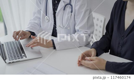 Doctor and a patient in clinic. The female physician is using laptop computer for filling up medication history record form, close up. Medicine and science Doctor and a patient in clinic. The female physician is using laptop computer for filling up medication history record form, close up. Medicine and science 117460174