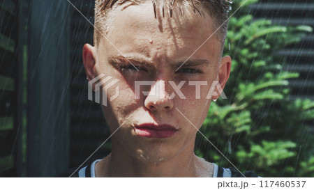 Raindrops running down the face of teen boy standing outside in the heavy rain 117460537