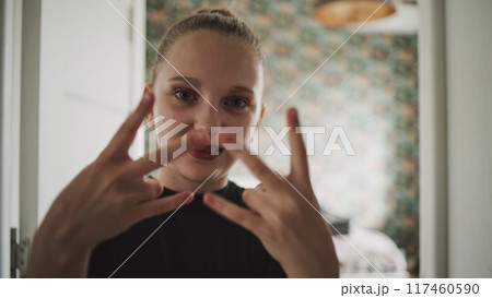 Adorable and happy young girl makes funny hand gestures on camera 117460590