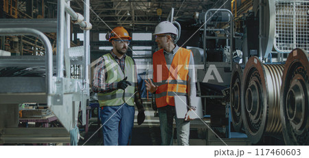 Two engineers discuss work process walking at manufacturing facility 117460603