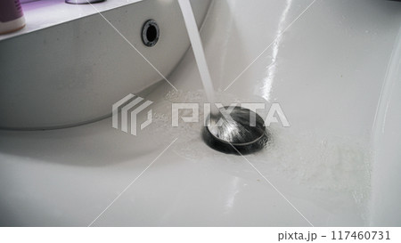 Clean bathroom sink with water pouring down on chrome stopper 117460731