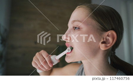 Young girl looks at mirror in bathroom, brushes her teeth 117460756