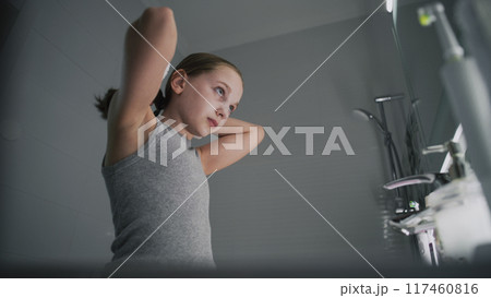Young girl looks at the mirror in bathroom and combs her hair 117460816