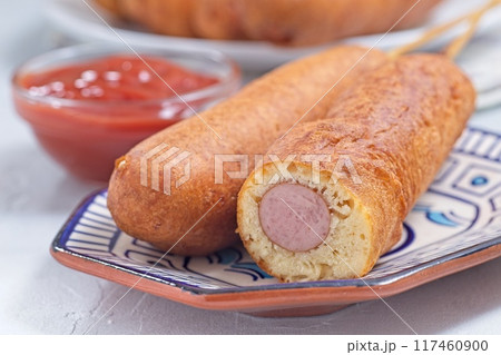 Corn dogs on white blue plate, served with ketchup, horizontal closeup Corn dogs on white blue plate, served with ketchup, horizontal closeup 117460900