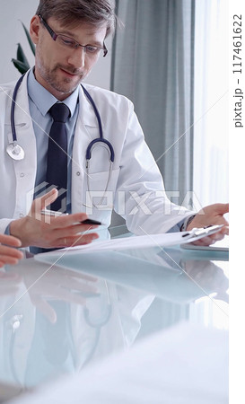 Doctor consulting patient. Male physician is pointing into medical records on a clipboard while talking with a woman in a clinic, close up. Medicine concept Doctor consulting patient. Male physician is pointing into medical records on a clipboard while talking with a woman in a clinic, close up. Medicine concept 117461622