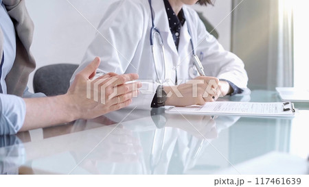 Doctor consulting patient in clinic. Female physician is writing notes while talking with a man, close up. Medicine concept Doctor consulting patient in clinic. Female physician is writing notes while talking with a man, close up. Medicine concept 117461639
