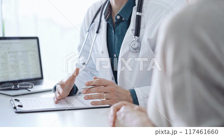 Doctor and a patient. The physician, wearing a white medical coat over a green shirt, is gesturing with his hands during a consultation in the clinic. Medicine 117461660