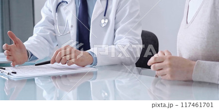 Doctor consulting patient. Male physician is pointing into medical records on a clipboard while talking with a woman in a clinic, close up. Medicine concept 117461701