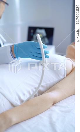Doctor man wearing blue protective gloves is using ultrasound equipment on the breast of a female patient. Mammary gland health. Medicine concept 117461824