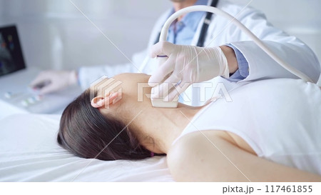 Doctor man is using ultrasound equipment on neck of female patient lying down for a medical examination. Medicine and science Doctor man is using ultrasound equipment on neck of female patient lying down for a medical examination. Medicine and science 117461855