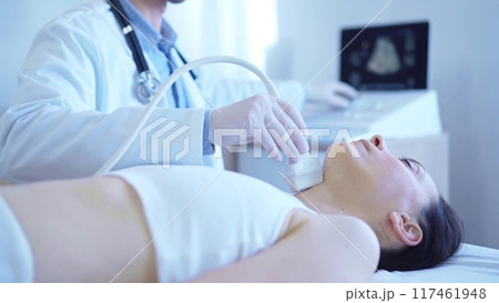 Doctor man with white medical gloves is using ultrasound machine to examine neck of female patient lying down in clinic. Medicine concept 117461948