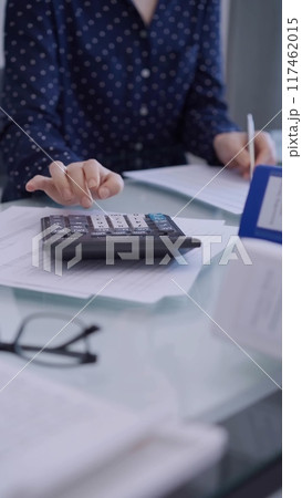 Female accountant is using a laptop computer and calculator for counting taxes at a glass desk in office. Woman in business audit and finance 117462015
