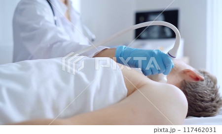 Doctor woman with a blue medic gloves performing neck ultrasound exam on male patient. Medicine service concept. Thyroid gland health Doctor woman with a blue medic gloves performing neck ultrasound exam on male patient. Medicine service concept. Thyroid gland health 117462031