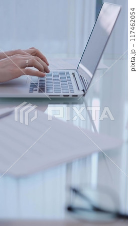 Business woman is working with laptop computer while sitting at the glass table in home office, closeup of hands 117462054