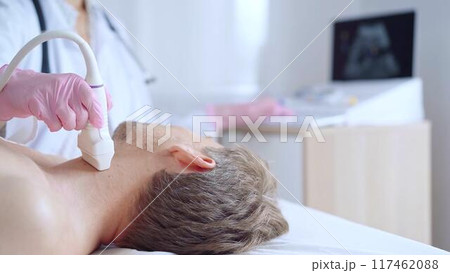 Doctor woman with pink medical gloves performing neck ultrasound exam on male patient. Thyroid gland examination. Medicine service concept Doctor woman with pink medical gloves performing neck ultrasound exam on male patient. Thyroid gland examination. Medicine service concept 117462088